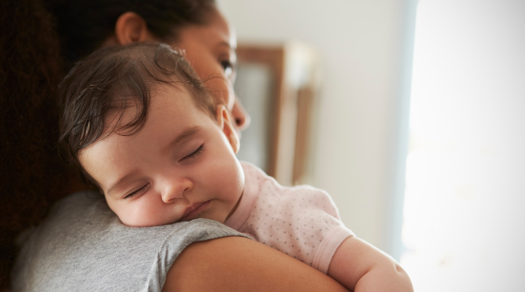 A sleeping baby rresting on the shoulder of her mother